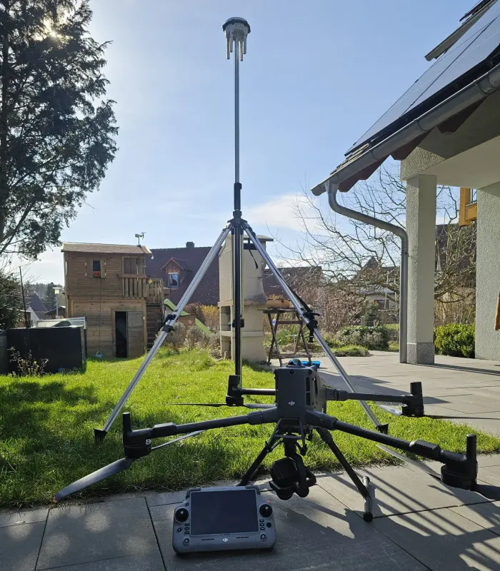 Vermessungsdrohne mit GNSS-Antenne und Fernsteuerung vor einem Haus